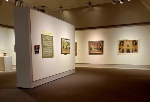 Art gallery interior featuring paintings on the walls and an informational display in the center.
