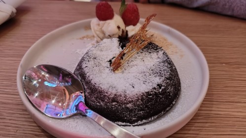 A chocolate lava cake dusted with powdered sugar, topped with a caramel shard, served with ice cream and raspberries.