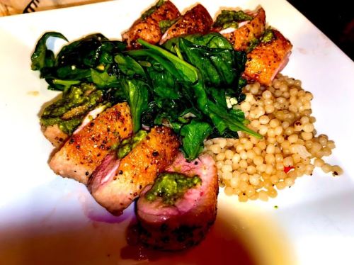 Sliced chicken with pesto, sautéed spinach, and pearl couscous on a white plate.