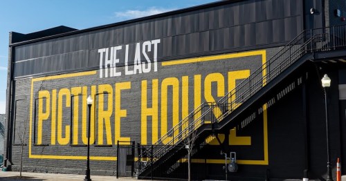 A black building with a large yellow sign reading "THE LAST PICTURE HOUSE" and an exterior staircase.