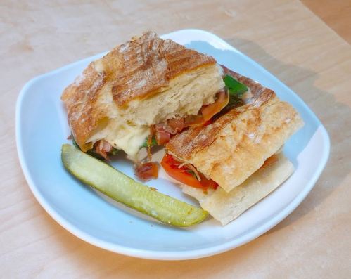 A sandwich with layers of meat, cheese, and vegetables, served on a plate with a pickle on the side.