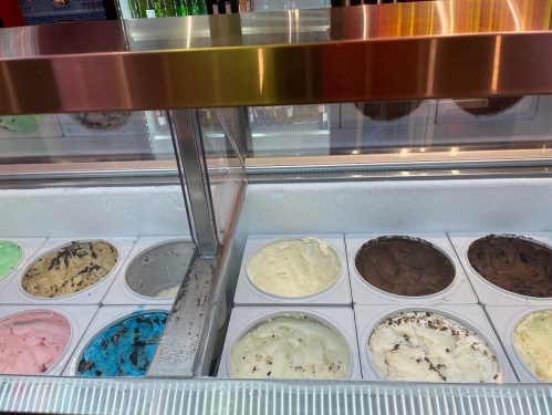 A display of various ice cream flavors in tubs, including mint green, pink, blue, white, and brown.