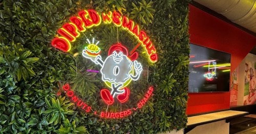 Neon sign of a cartoon character holding a burger, surrounded by greenery, with the text "Dipped N Smashed" above.