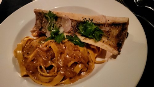 A plate of fettuccine pasta topped with a rich sauce and a bone marrow garnish, sprinkled with herbs.