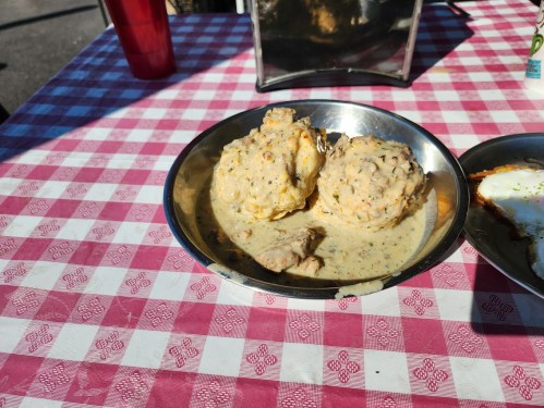 A metal bowl with two large dumplings in creamy sauce, served on a red and white checkered tablecloth.