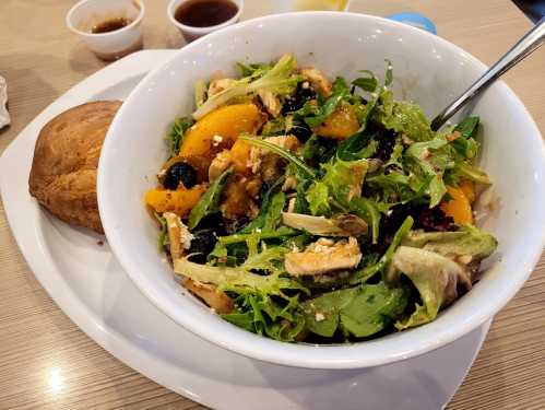 A large bowl of mixed salad with greens, chicken, and fruit, accompanied by a biscuit and small containers of dressing.