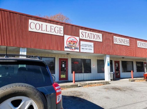 Exterior of a business center with a sign for "College Station" and "Bodega Grill," featuring an open sign in the window.