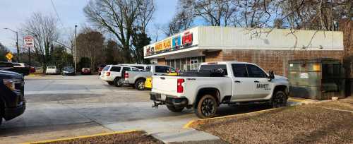 A parking lot with several vehicles, including a white truck, near a convenience store and a dumpster.