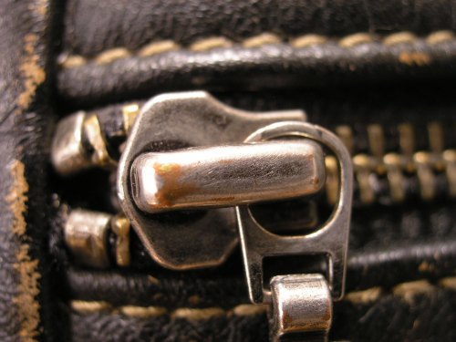 Close-up of a metal zipper on a black leather surface, showcasing the teeth and slider mechanism.