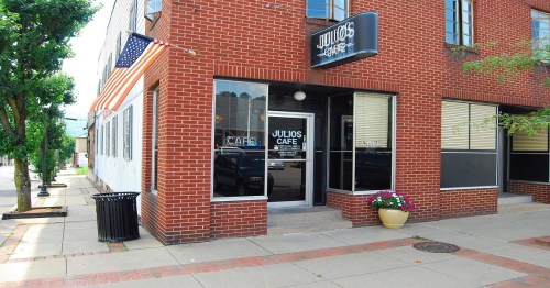 Exterior of Julio's Cafe, a brick building with large windows, an American flag, and potted flowers at the entrance.