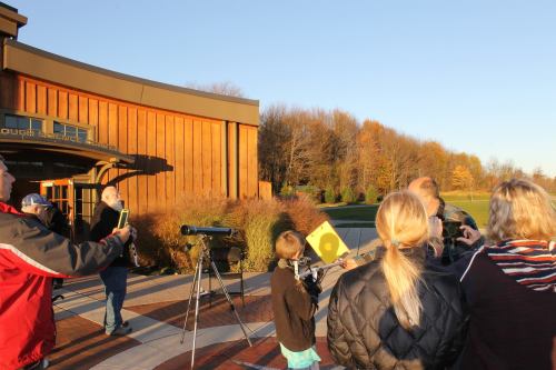 People observing the sky with telescopes outside a science center on a clear autumn day.