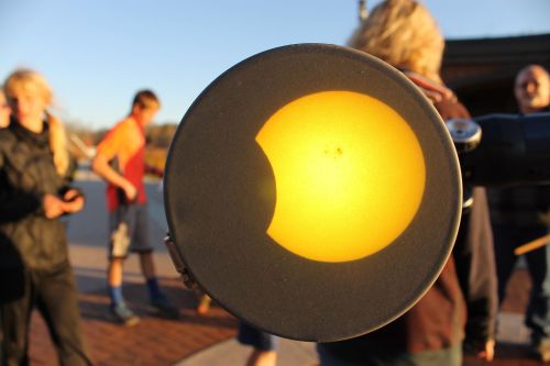 A solar eclipse viewed through a telescope, with people gathered in the background.