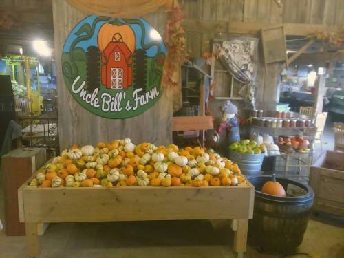 A wooden display filled with various pumpkins and gourds, with a colorful sign for Uncle Bill's Farm in the background.