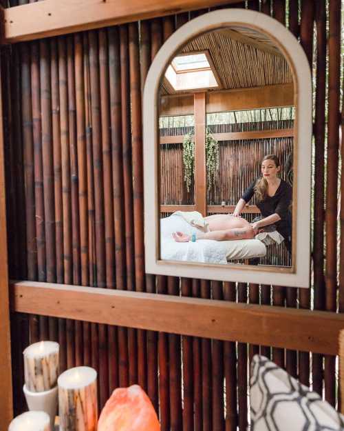 A serene spa setting with a therapist giving a massage, reflected in a mirror surrounded by bamboo walls.