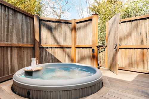 A private outdoor hot tub surrounded by wooden fencing and greenery, with a pitcher on a small tray beside it.