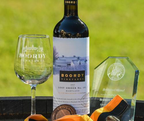 A bottle of Boordy Vineyards wine, a glass, an award plaque, and a medal on a table with a green background.