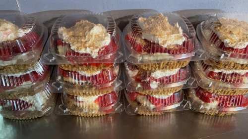 Stacked dessert containers filled with layers of strawberries, cream, and crumb topping.