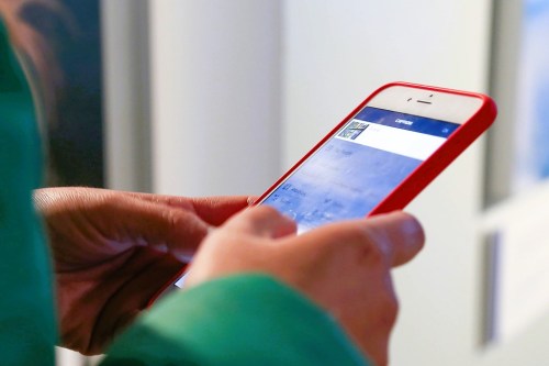 A person holding a red smartphone, looking at a screen with a blurred image and text.