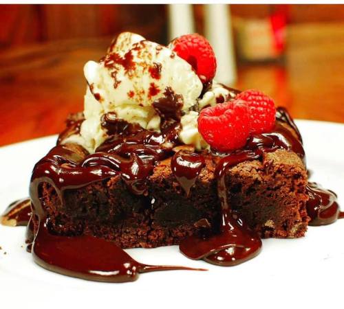 A decadent chocolate brownie topped with vanilla ice cream, chocolate sauce, and fresh raspberries on a white plate.