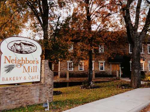 A cozy bakery and café with a sign reading "Neighbor's Mill," surrounded by autumn foliage and a peaceful setting.