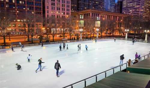 A bustling outdoor ice skating rink in a city, with people skating and enjoying the evening lights.