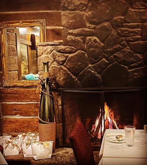 Cozy restaurant interior with a stone fireplace, a decorative mirror, and gift boxes on a table.