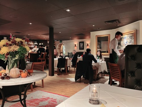 A cozy restaurant interior with diners at tables, a bar in the background, and autumn decorations on the table.