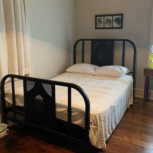 A simple bedroom featuring a black metal bed frame, white bedding, and a small nightstand with a lamp.