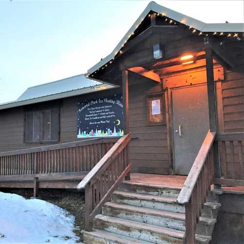 A wooden building with a sloped roof, featuring a welcoming entrance and holiday lights, surrounded by snow.