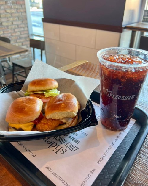A tray with three mini burgers and a large soda on a table in a casual dining setting.