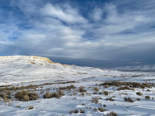Snow-covered landscape with rolling hills and a cloudy sky, showcasing a serene winter scene.