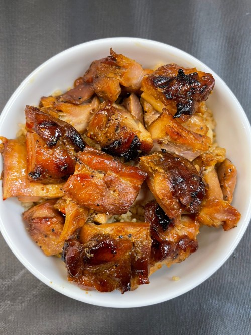 A bowl of grilled chicken pieces, caramelized and glazed, served over a bed of rice.