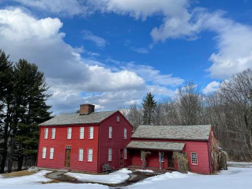 A red two-story house with a gray roof, surrounded by snow and trees, under a partly cloudy sky.