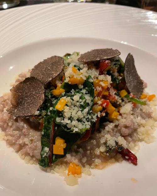A gourmet dish featuring grains topped with sautéed greens, colorful vegetables, and slices of truffle.