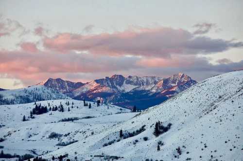 Snow-covered mountains under a pink and purple sky, with rolling hills in the foreground.