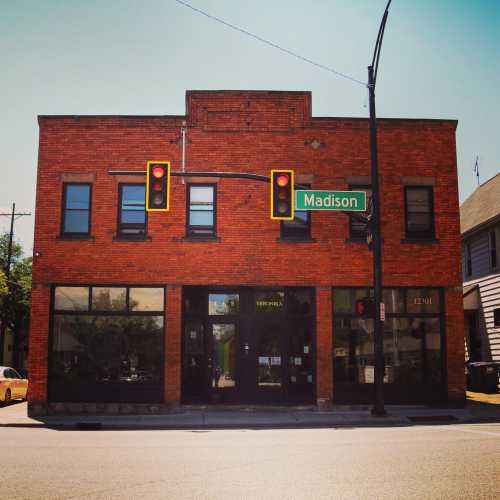 Red brick building at an intersection with traffic lights and a street sign for Madison. Clear blue sky above.