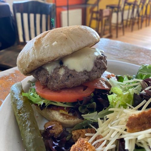 A juicy cheeseburger with lettuce, tomato, and pickles, served with a side salad on a wooden table.