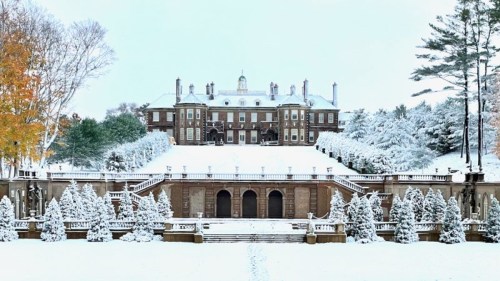 A grand mansion surrounded by snow-covered trees and a winter landscape, with a staircase leading to the entrance.