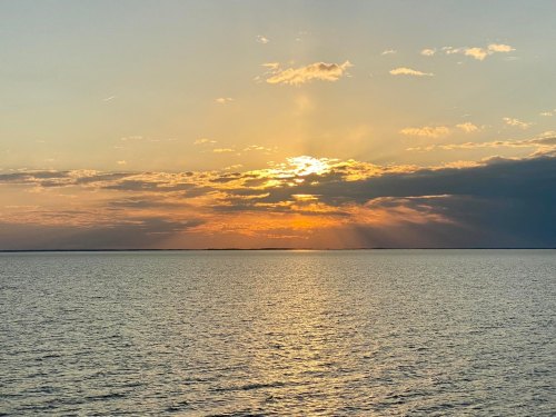 A serene sunset over calm waters, with golden rays breaking through clouds and reflecting on the surface.
