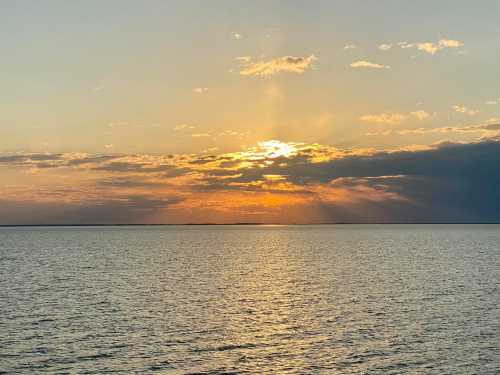 A serene sunset over calm waters, with golden rays breaking through clouds and reflecting on the surface.