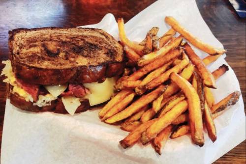 A hearty sandwich on toasted bread served with a side of crispy sweet potato fries.