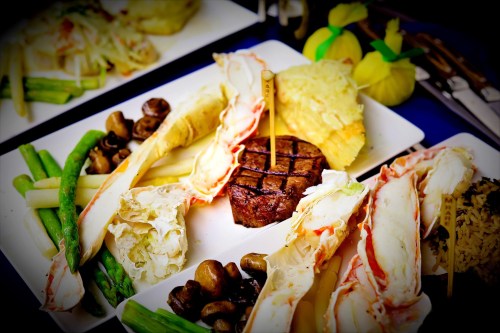 A gourmet plate featuring grilled steak, crab legs, asparagus, mushrooms, and garnishes, beautifully arranged.