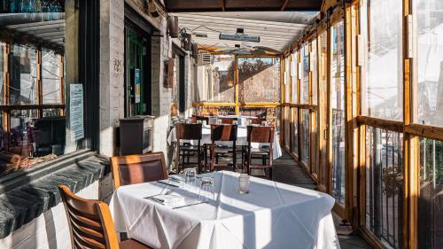 A sunlit restaurant patio with empty tables set for dining, surrounded by wooden railings and glass panels.
