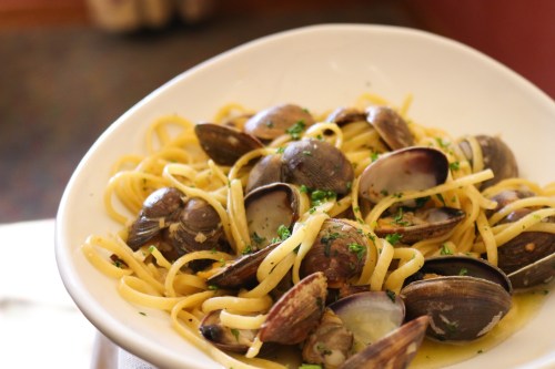 A bowl of linguine pasta topped with clams and garnished with parsley.