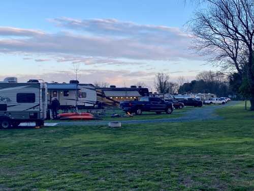 A campsite with several RVs and trucks parked on a grassy area, under a cloudy sky at dusk.