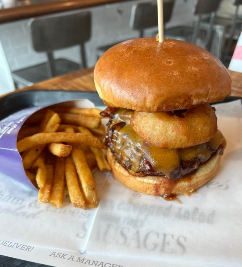 A stacked burger with cheese and crispy onion rings, served with a side of golden French fries on a tray.