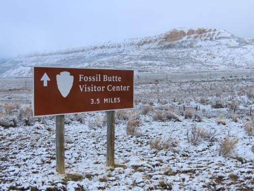 Sign for Fossil Butte Visitor Center, indicating it's 3.5 miles away, with a snowy landscape in the background.