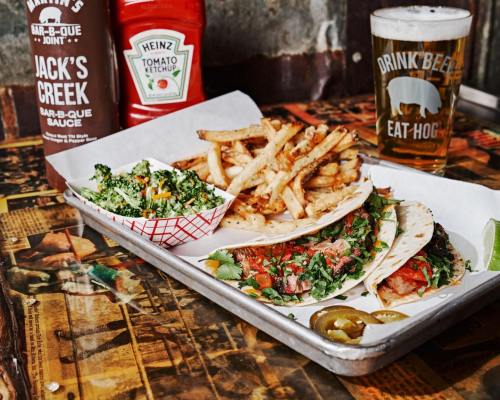 A tray with tacos, fries, and a side salad, accompanied by a beer and ketchup on a rustic table.