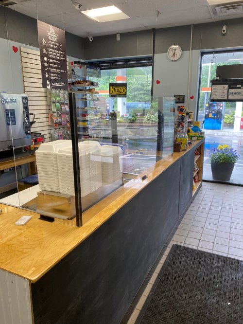 A counter in a shop with a clear divider, stacks of takeout containers, and a view of the entrance and display area.