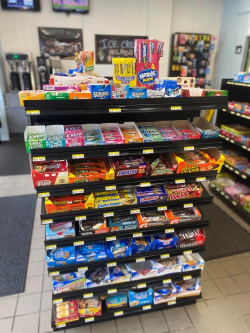 A display rack filled with various candy and snack options, including chocolate bars and gummies, in a convenience store.